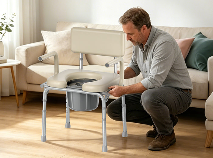 A man assembles a padded drop-arm bedside commode in a living room.